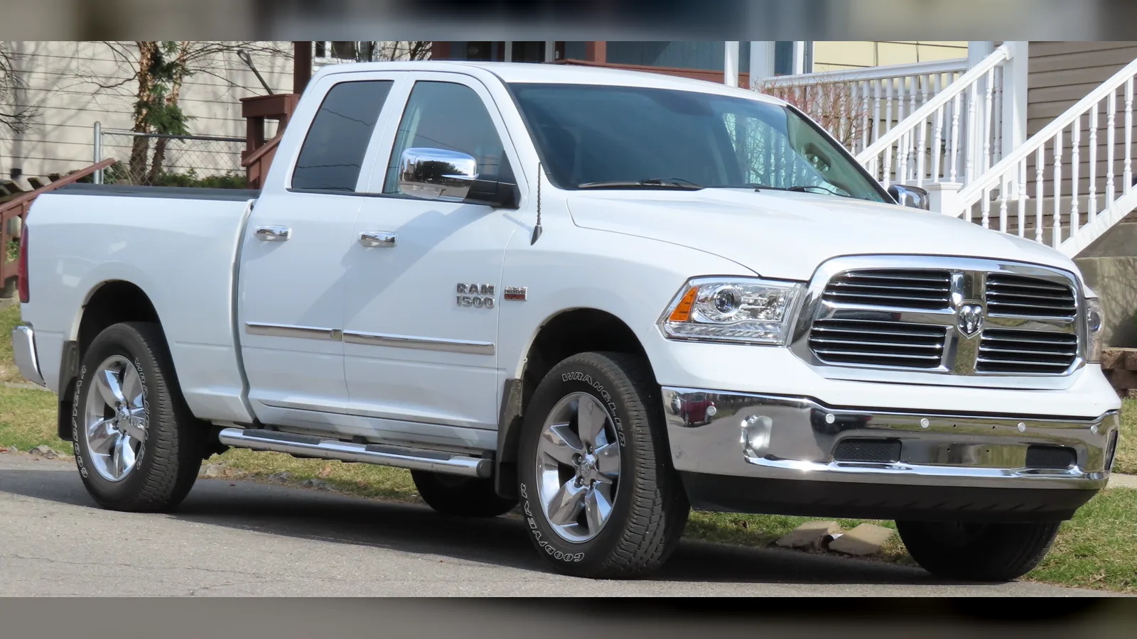 White 2013-2018 Ram 1500 Quad Cab pickup, front three-quarter view, parked by a house