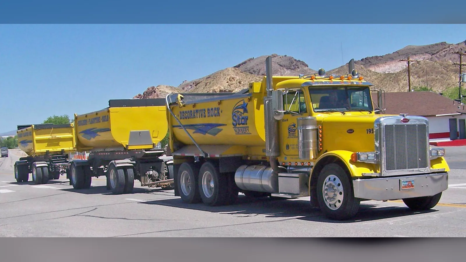 Yellow Peterbilt dump truck with two trailers, on a road