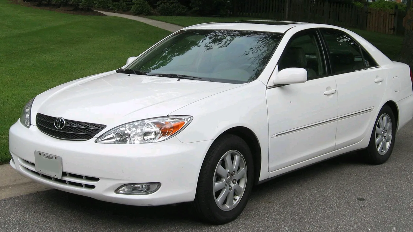 White 2002-2004 Toyota Camry sedan, front three-quarter view, parked by a lawn
